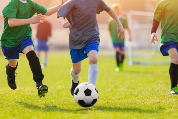 Running Soccer Football Players During the Sunrise. Footballers Kicking Football Match. Soccer School Tournament. Young Soccer Players Running After the Ball. Soccer Stadium in the Background